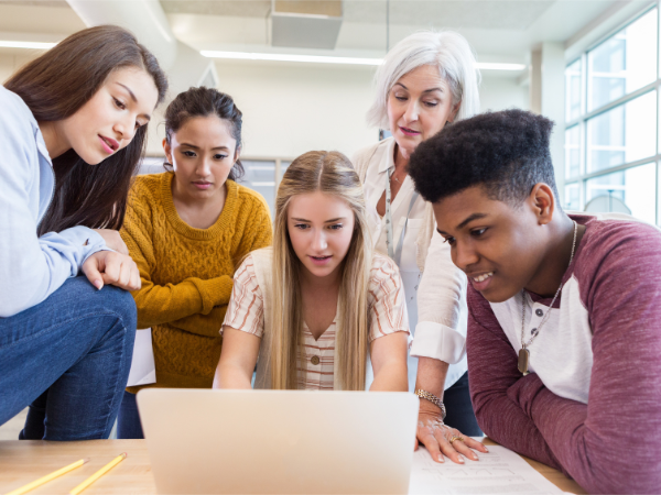 A student sitting in front of a laptop using ChatGPT ethically and responsibly while classmates and a teacher watch