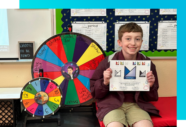 A student holding a math achievement certificate and sitting in front of prize wheels used for math motivation.